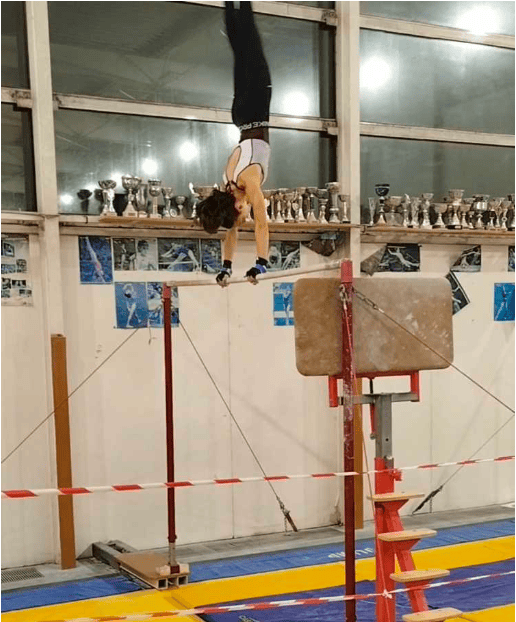 Gymnaste en équilibre renversé (mouvement « soleil ») sur une barre, en salle de gymnastique