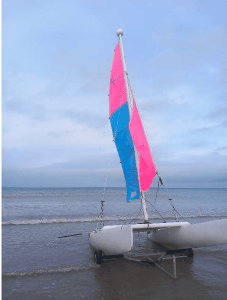Catamaran de plage aux voiles rose et bleu sur le rivage, support de l'étude sur l'angle de voile