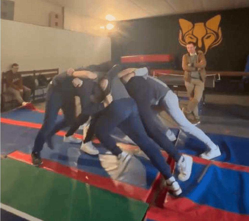 Élèves s'entraînant à une mêlée de rugby sur des tapis, dans un gymnase