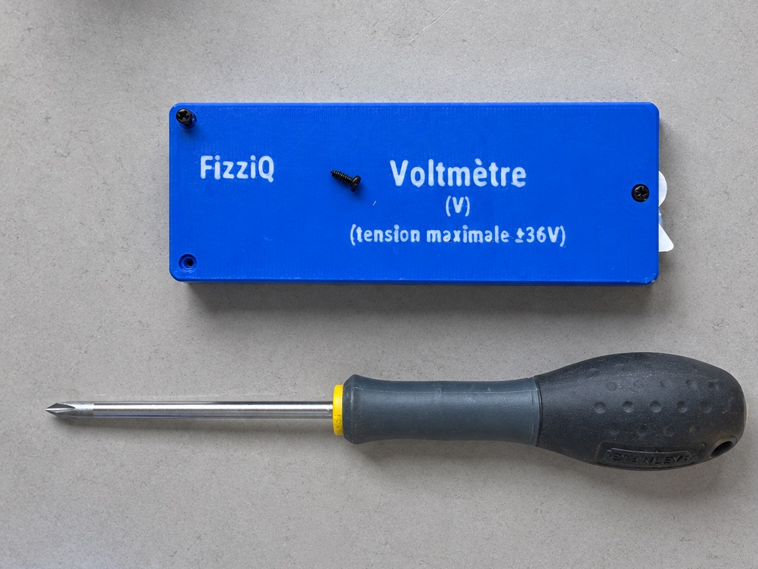 Boîtier Voltmètre FizziQ Connect refermé et vissé, tension maximale ±36 V, à côté d'un tournevis cruciforme