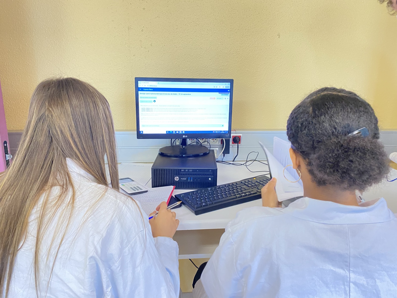 Deux élèves en blouse suivant un TP de chimie sur FizziQ Web à l'ordinateur