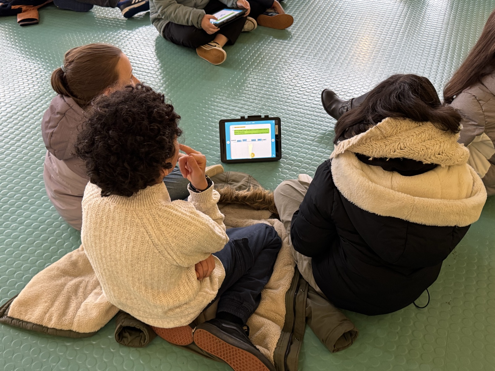 Élèves regroupés autour d'une tablette pour une activité FizziQ sur le son