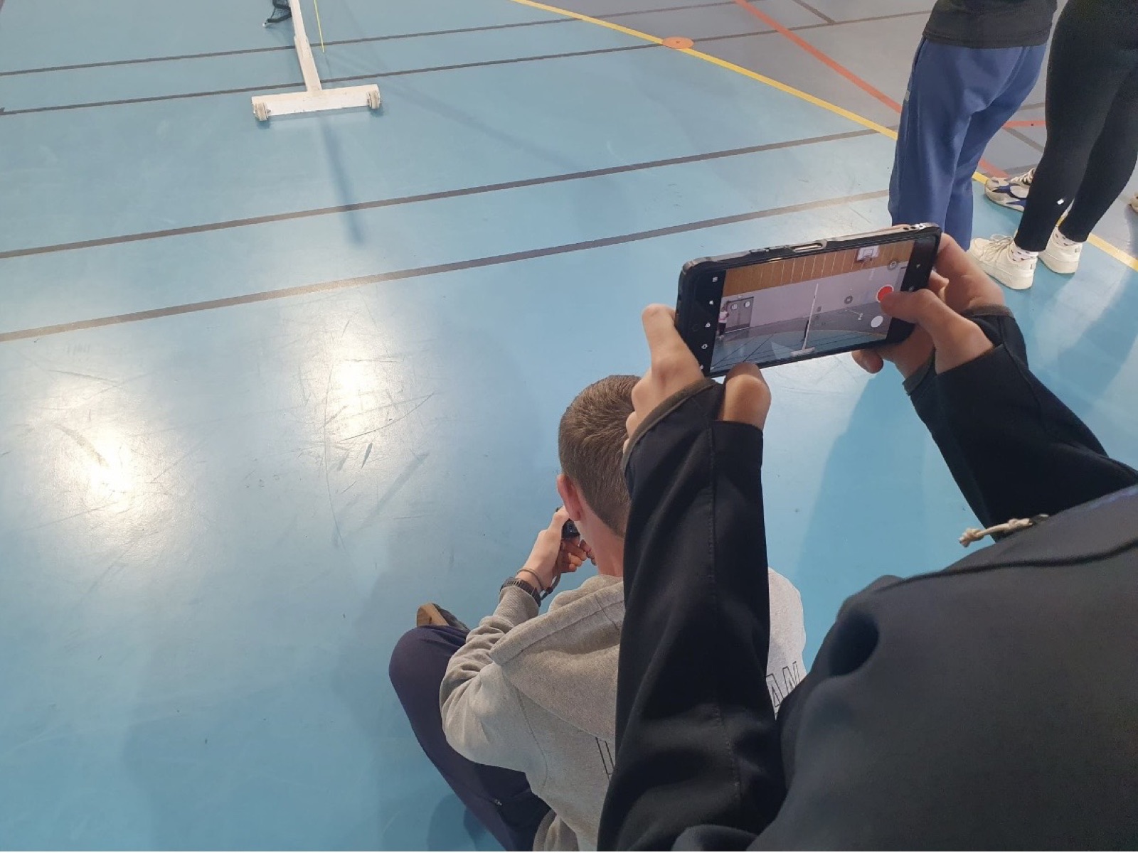 Élève filmant un mouvement au gymnase avec un smartphone pour l'analyse vidéo