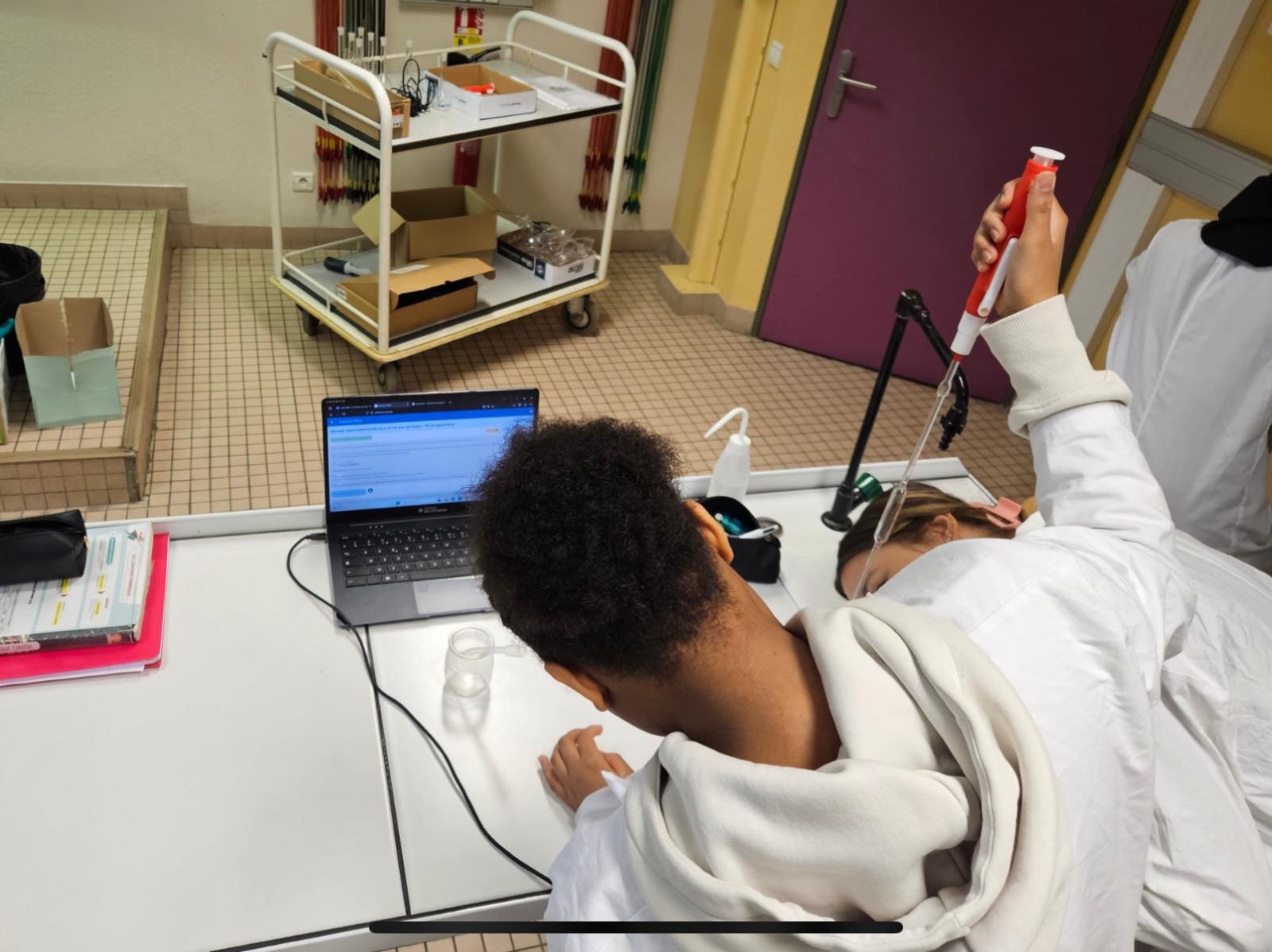 Élève en blouse utilisant une micropipette en TP de chimie, FizziQ Web sur l'ordinateur